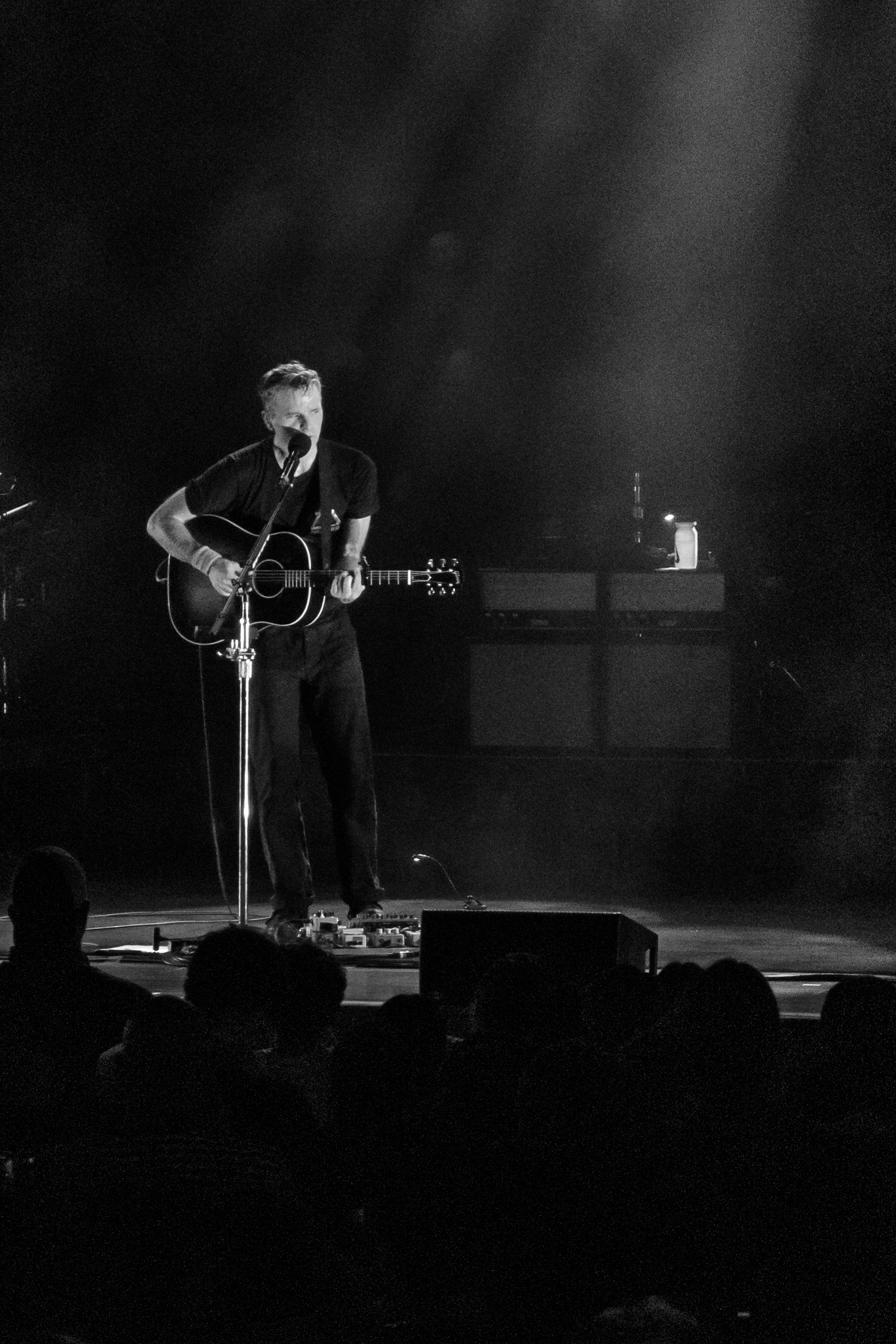 Ben Gibbard alone at center stage with an acoustic guitar, lit by a single spotlight.